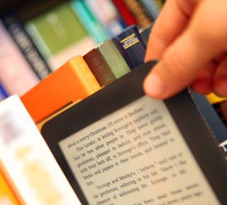 Hand taking a small tablet computer from a row of books
