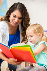 Toddler age girl reading to nursery teacher