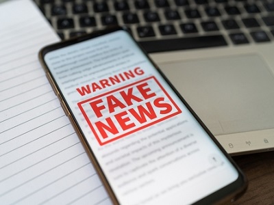 Photo of a computer screen displaying digital news articles with a magnifying glass hovering over the text, symbolizing AI technology detecting fake news online.