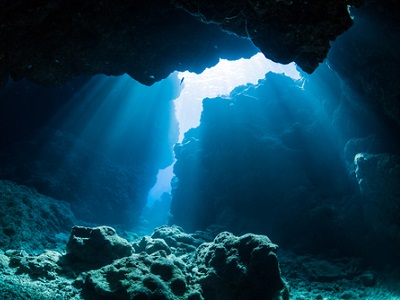 Underwater cave with light streaming through, representing the deep-sea environment where AI is now being used to explore volcanoes and ocean data.