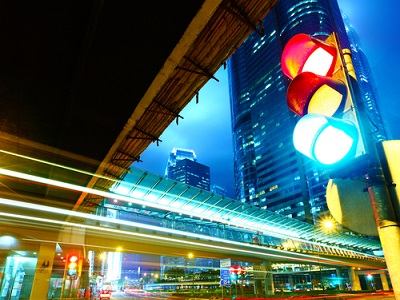 A brightly lit urban scene with smart traffic lights showing red, amber, and green signals simultaneously, set against a modern cityscape and glass buildings at night.