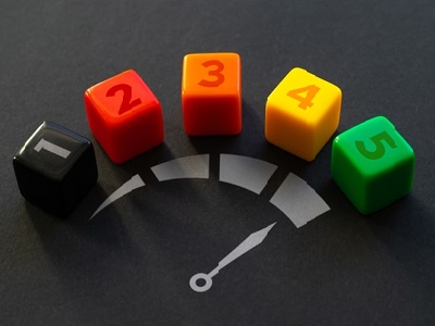 A row of five coloured dice numbered 1 to 5, placed above a printed speedometer graphic, symbolising progress or an upgrade.