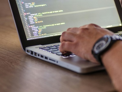 Close-up of a person’s hands typing on a laptop keyboard with computer code displayed on the screen, symbolising programming and AI coding work.