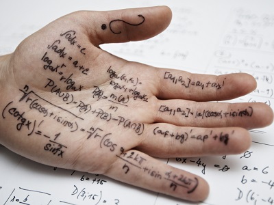 A close-up of a human hand covered in handwritten maths formulas, representing exam cheating, with a blurred page of calculations in the background.