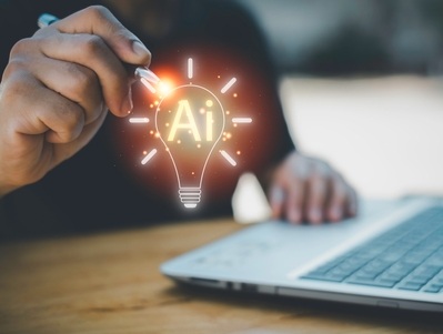 A person holding a pen near a glowing lightbulb icon labeled “AI” in front of a laptop, symbolizing a bright idea related to artificial intelligence.