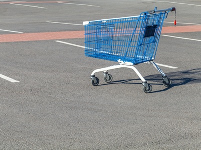 A single blue shopping trolley left in the middle of an empty supermarket car park, looking lonely on the asphalt.