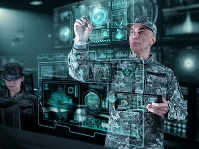 Two soldiers in digital camouflage working in a high-tech control room, with transparent holographic screens and dashboards; senior officer using a touch interface—concept of AI-assisted defence operations.