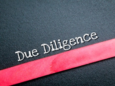 Close-up of the words “Due Diligence” on a dark textured surface with a bold red line running diagonally across, suggesting careful checks and clear boundaries.