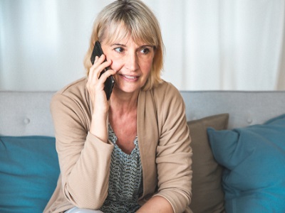 Middle-aged woman sitting on a sofa, holding a mobile phone to her ear, looking concerned while waiting during a phone call.