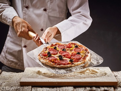 A chef slicing a freshly baked pepperoni pizza on a wooden surface. The pizza has a perfectly crispy crust and is topped with slices of pepperoni, olives, and cheese, ready to be served.