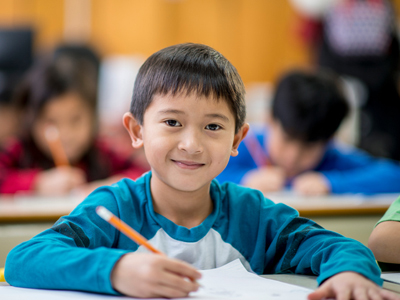 Schoolboy writing at desk in class