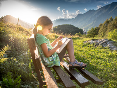 Girl on bench writing with moutain backdrop