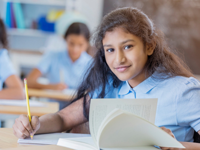 Schoolgirl with research book sitting at desk