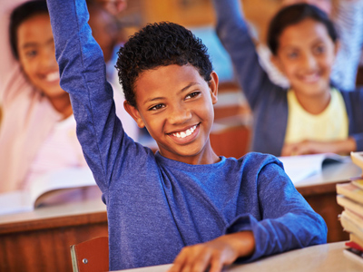 Grade 5 schoolboy with hand raised in class