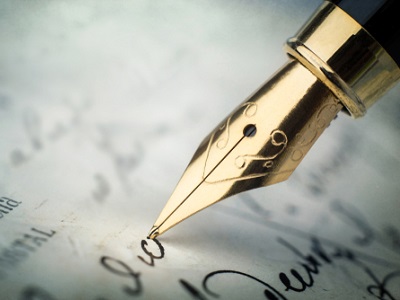A gold-nibbed fountain pen writing on parchment paper.