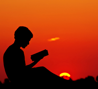 Silhouette of a boy reading at sunset
