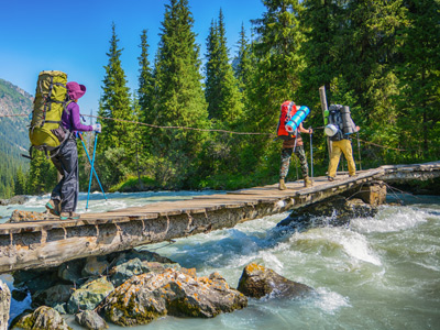 Hikers crossing river by rickety bridge