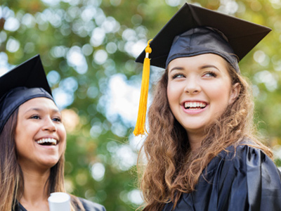 Happy teenage girls wearing graduation gowns and mortar boards