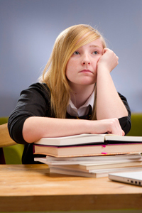 Bored teenage schoolgirl doing homework and leaning on textbooks