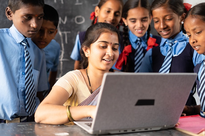 Teacher at computer with students crowded around her