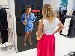 A woman stands in front of a virtual mirror in a clothing store, trying on a blue satin dress. The AI mirror displays the dress with a price tag, while she looks at her reflection, holding a handbag.