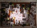 A corkboard covered in crime scene photos, handprints, fingerprints, newspaper clippings, and maps connected by red string, resembling a detective investigation wall.