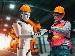A humanoid robot and a human worker wearing safety helmets and vests stand in a high-tech factory, reviewing a tablet together in front of robotic machinery.