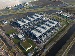 Aerial view of a large industrial data centre surrounded by green fields, canals, and roads, showing cooling units, infrastructure buildings, and nearby farmland.