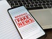 Photo of a computer screen displaying digital news articles with a magnifying glass hovering over the text, symbolizing AI technology detecting fake news online.