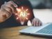 A person holding a pen near a glowing lightbulb icon labeled “AI” in front of a laptop, symbolizing a bright idea related to artificial intelligence.