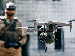 A close-up of a military-grade drone carrying equipment, with a soldier in camouflage gear blurred in the background, representing AI use in defence operations.