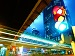 A brightly lit urban scene with smart traffic lights showing red, amber, and green signals simultaneously, set against a modern cityscape and glass buildings at night.