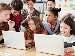 Group of school pupils using laptops at a classroom table while a teacher watches and supports their work.