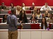 A lecturer speaking to university students seated in a tiered lecture theatre, with students listening and taking notes.