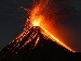 A night-time photograph of a volcano erupting, with bright orange lava shooting into the air and glowing streams flowing down the mountain, symbolising volcanic activity and seismic monitoring.