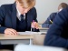 A secondary school student in a blue uniform uses a compass and pencil to complete a maths diagram in a classroom.