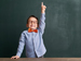 Boy in bowtie with hand up against blackboard
