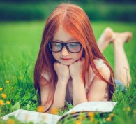 Young girl lying in the grass and reading a book